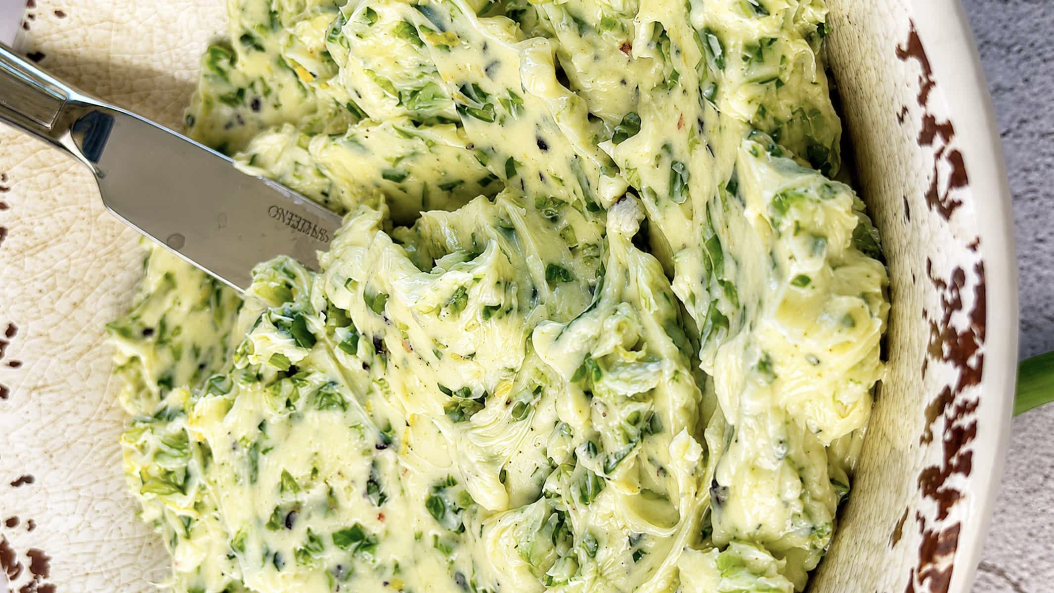 Close up of creamy garlic scape butter with chopped garlic scapes in a rustic serving bowl.