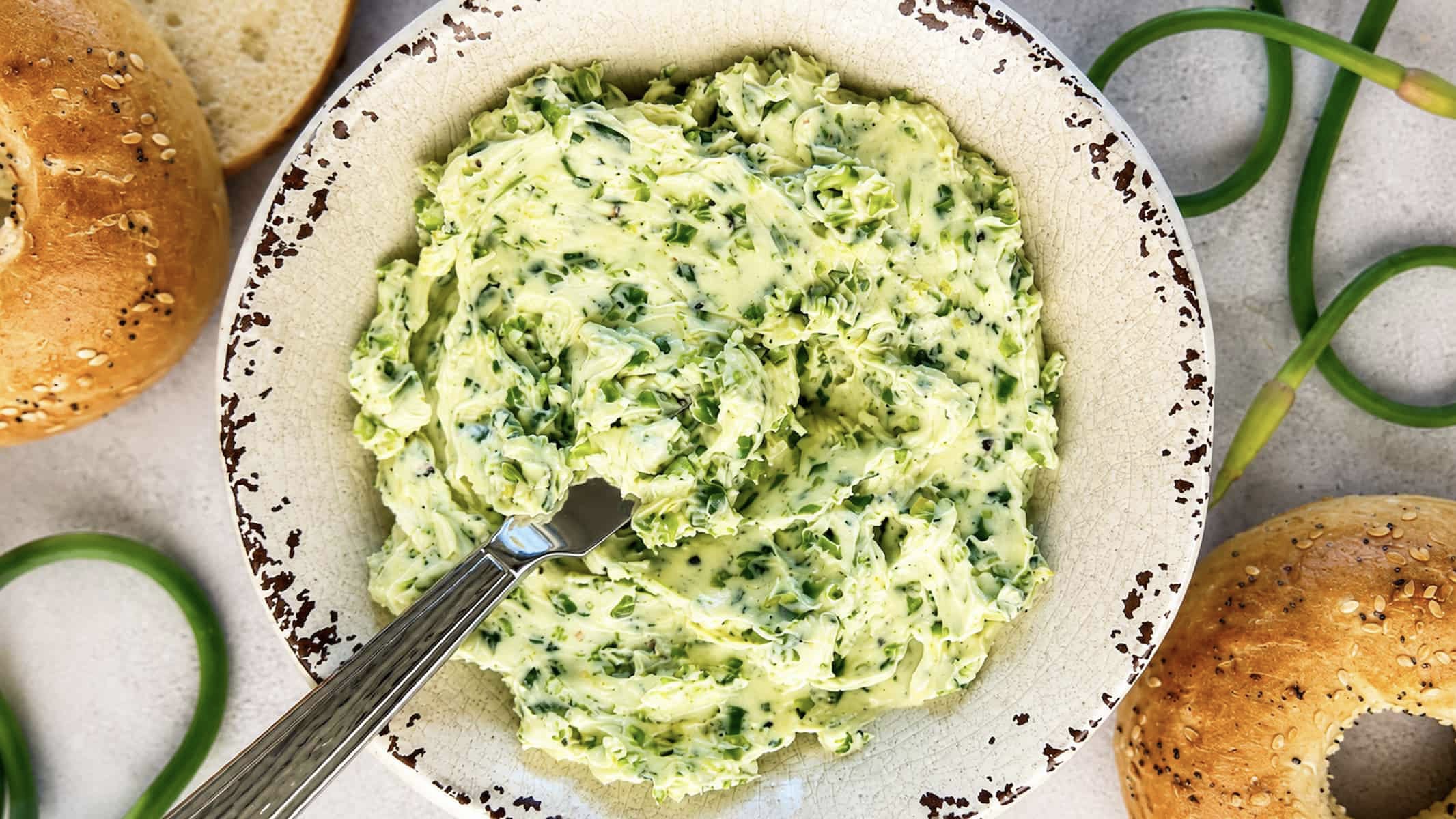 Garlic scape butter in a rustic bowl with fresh garlic scapes and everything bagels.