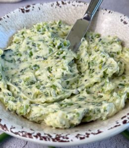 Creamy garlic scape butter with chopped garlic scapes in a rustic serving bowl with a butter knife.