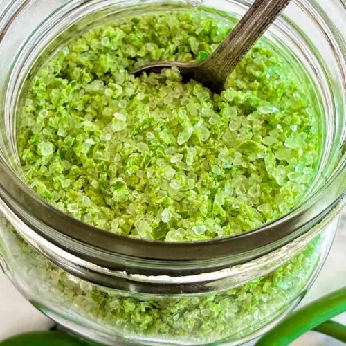 Garlic scape salt in a glass jar with coarse sea salt crystals and a small wooden spoon.
