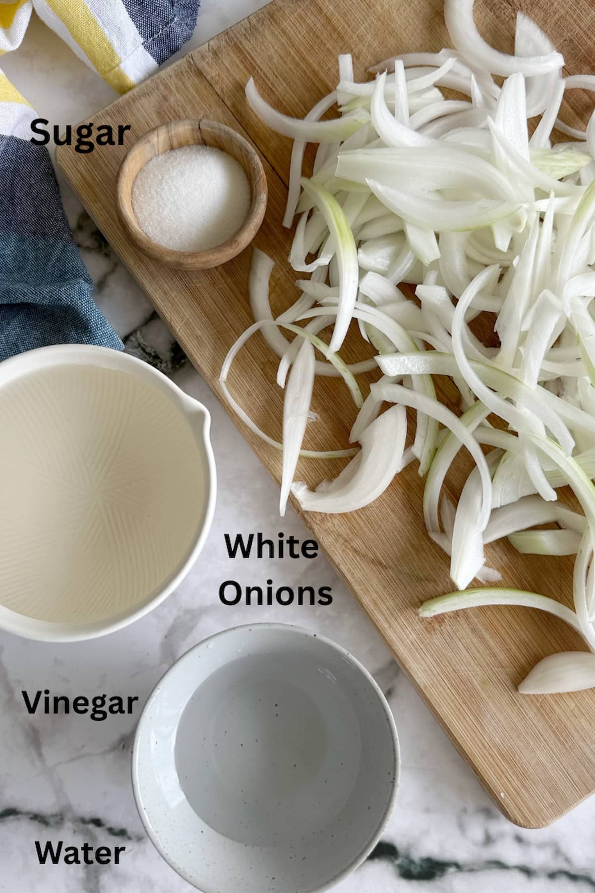 ingredients for pickled white onions recipe - sliced white onions on a cutting board, sugar, vinegar, and water.