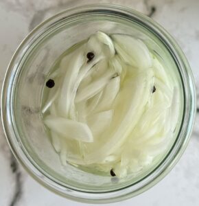 sliced white onions in a peppercorn brine in a glass jar.