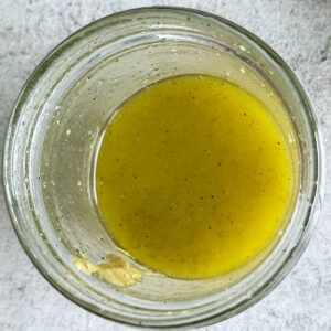 yellow olive oil based salad dressing with seasonings in a glass jar.