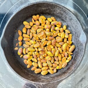 whole pistachios toasting in a small cast iron skillet on a burner.