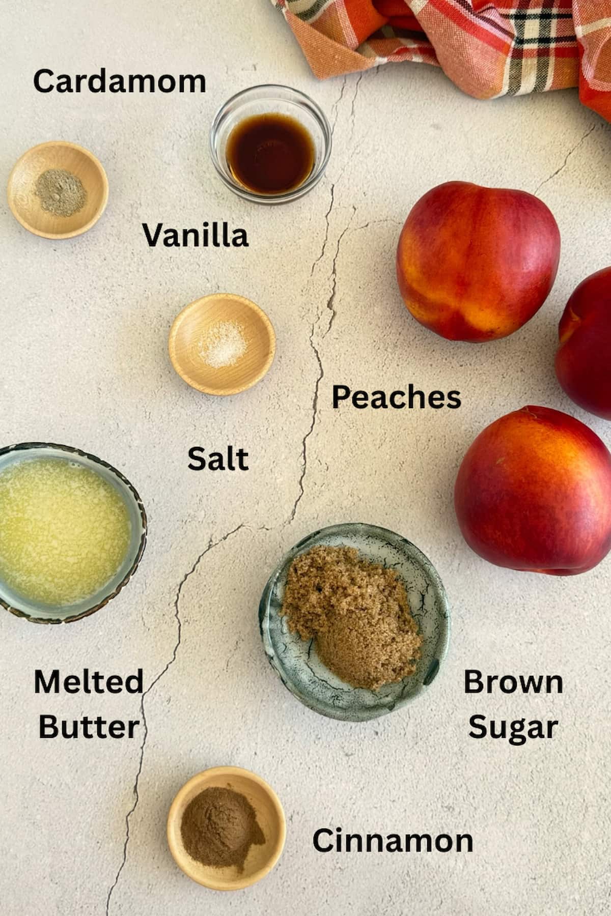 ingredients for air fryer peaches laid our in small bowls next to 3 whole peaches - melted butter, cinnamon, cardamom, salt, vanilla, and brown sugar.