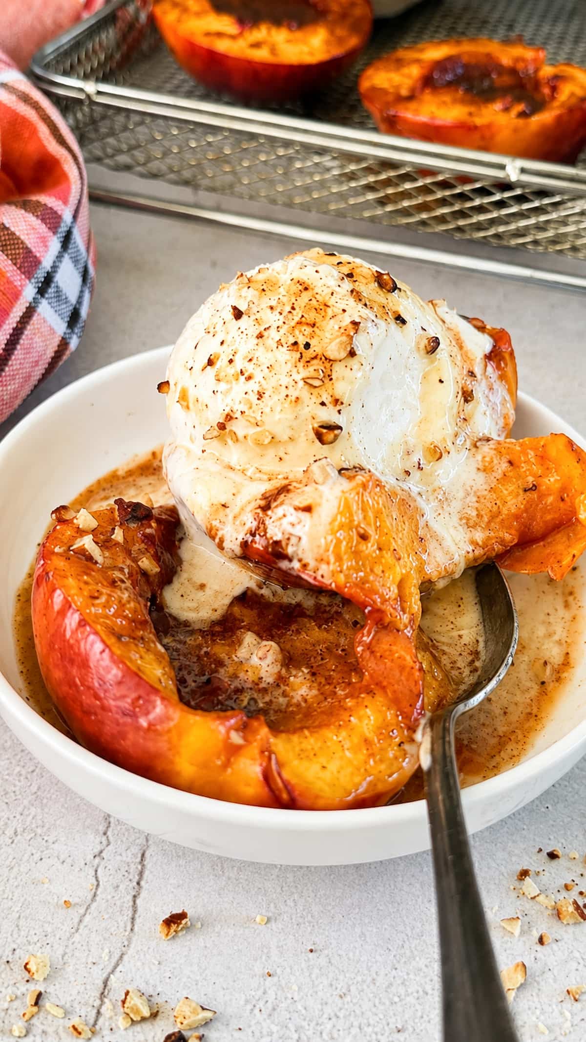 Air fryer peaches topped with vanilla ice cream, cinnamon, and chopped nuts.