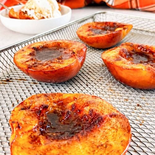 Air fryer peach halves caramelized with cinnamon and brown sugar on an air fryer basket.