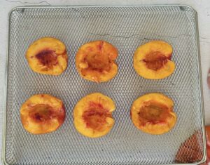 6 peach halves face up on an air fryer basket.