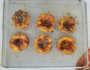 6 peach halves with brown sugar crumbles and brown sugar glaze on an air fryer basket.