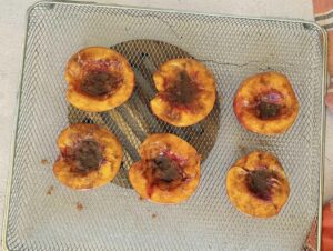 6 caramelized peach halves on an air fryer tray.