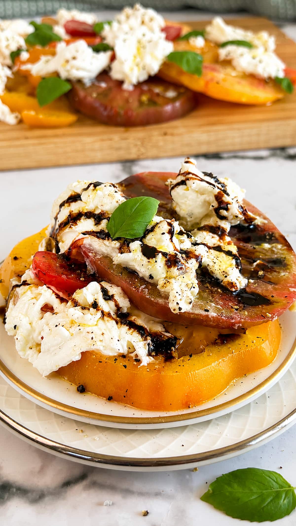 Plated Burrata Caprese salad with heirloom tomatoes, creamy burrata, fresh basil, and balsamic glaze, with a serving board of additional Caprese salad in the background.