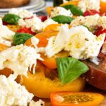 Close up of Burrata Caprese salad with creamy burrata, heirloom tomatoes, cherry tomatoes, fresh basil, and olive oil on a wooden serving board.