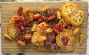 sliced dark red and yellow heirloom tomatoes and mixed coloured cherry tomatoes on a wooden cutting board.