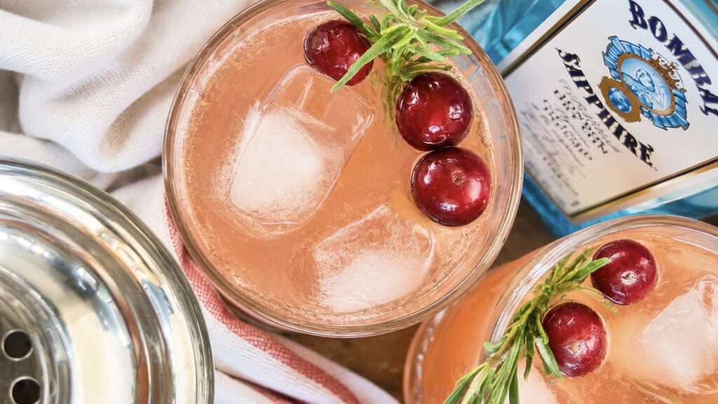 Cranberry gin fizz cocktails garnished with fresh cranberries and rosemary sprigs over ice.