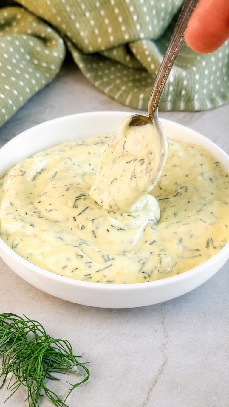 Creamy dill mayonnaise in a white bowl with fresh chopped dill and a spoon lifting a dollop.