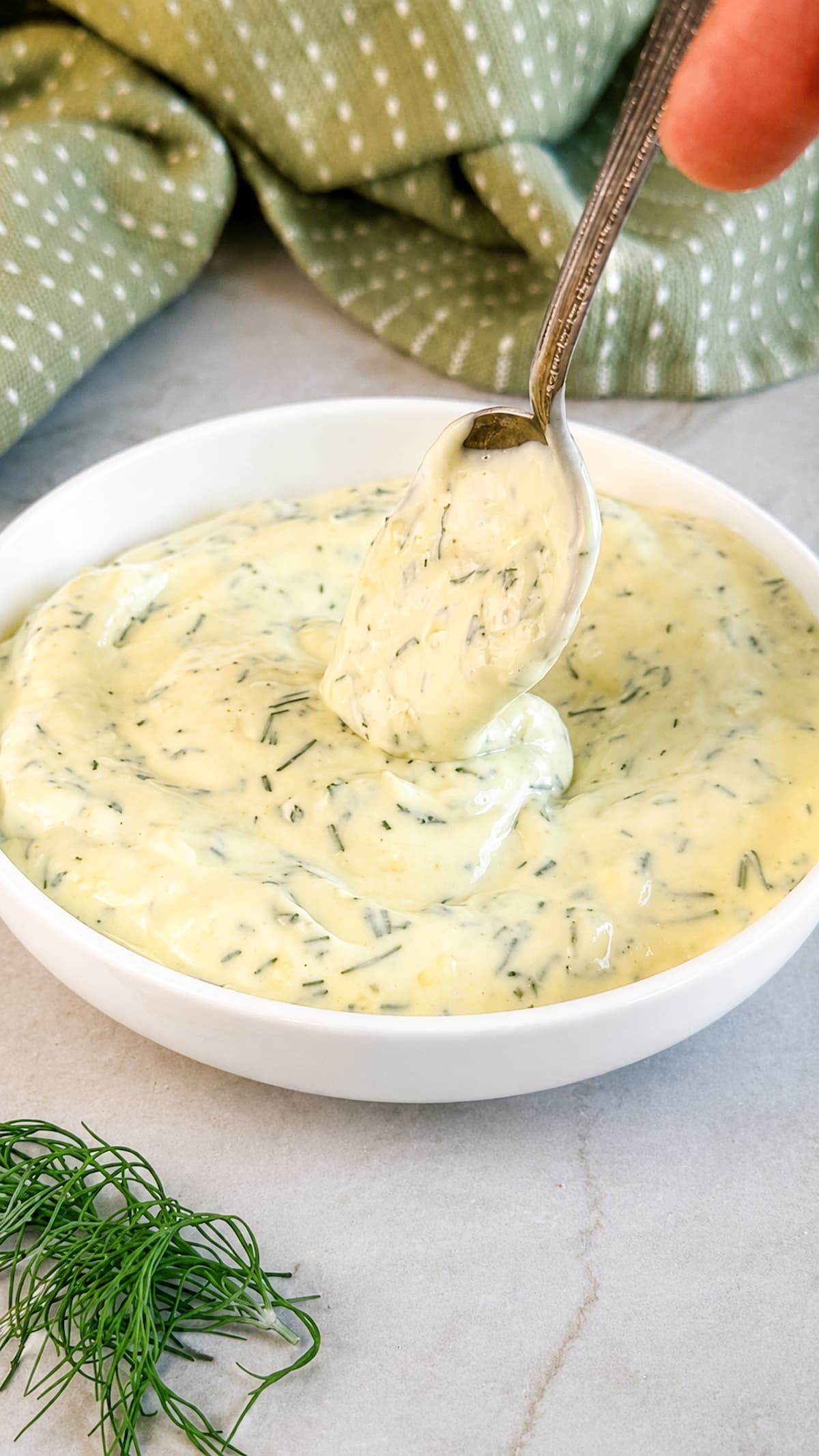 Creamy dill mayonnaise in a white bowl with fresh chopped dill and a spoon lifting a dollop.