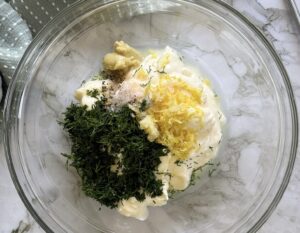 fresh dill, mayonnaise, lemon zest, garlic, dijon mustard, lemon juice, salt, and pepper unmixed in a glass bowl.