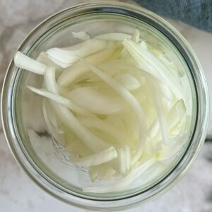 thinly sliced white onions piled into a mason jar.