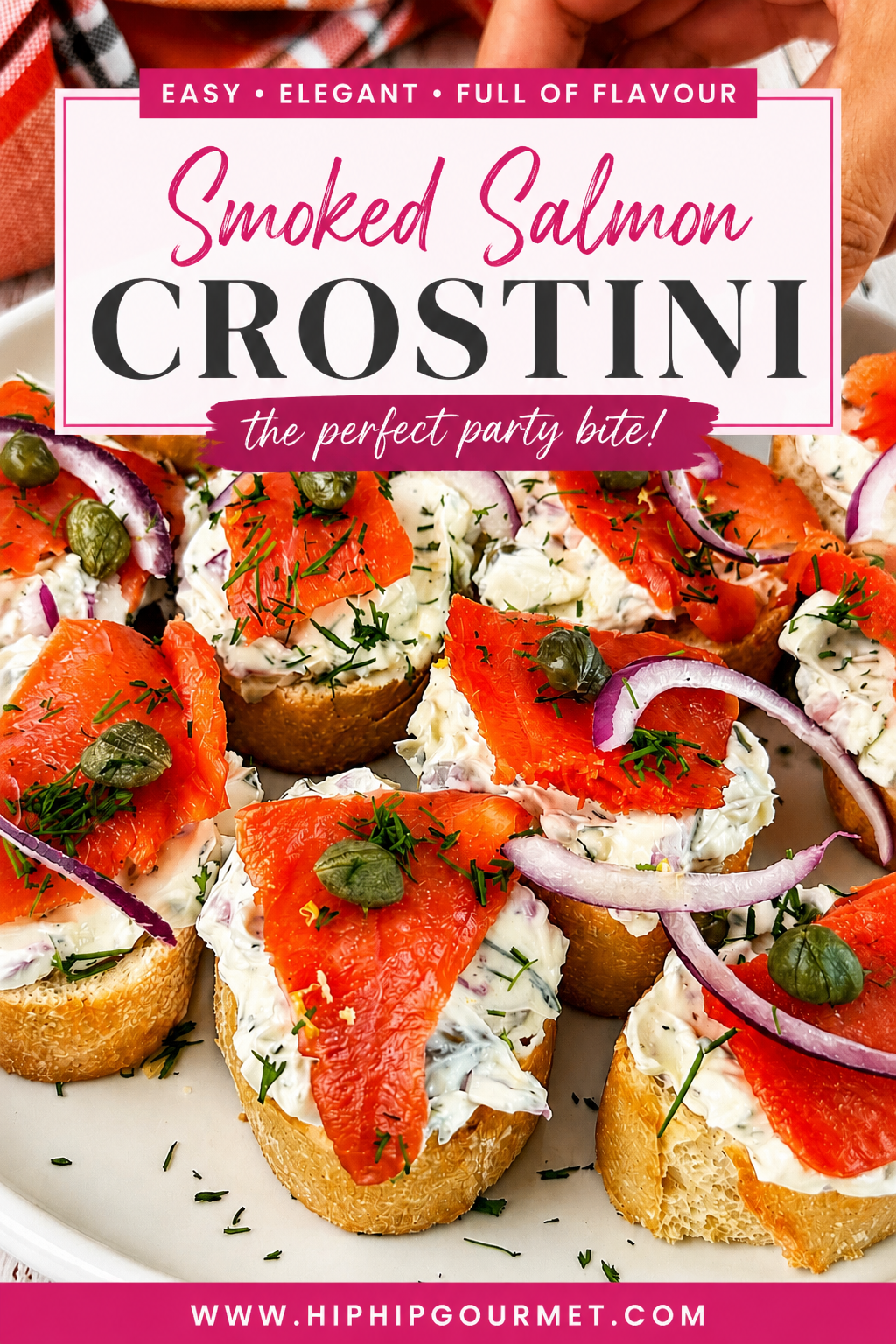 Hand reaching for smoked salmon crostini topped with herbed cream cheese, red onion, capers, and fresh dill.