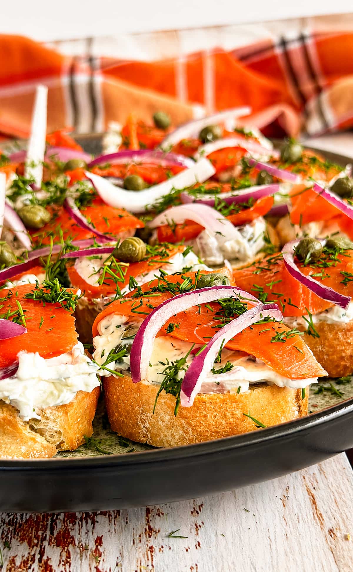 Smoked salmon crostini with herbed cream cheese, red onion, capers, and fresh dill on a serving platter.