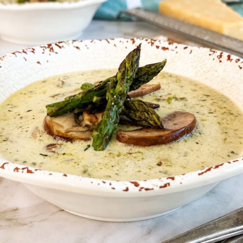 Creamy mushroom and asparagus soup topped with sautéed mushrooms and roasted asparagus in a rustic white bowl.