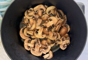 cooked/browned sliced mushrooms in a black dutch oven pot.