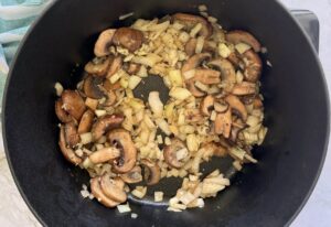 sliced mushrooms, onions, and garlic cooking in a black pot.