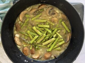 pot of broth with sliced mushrooms, chopped asparagus, onions, and other ingredients.