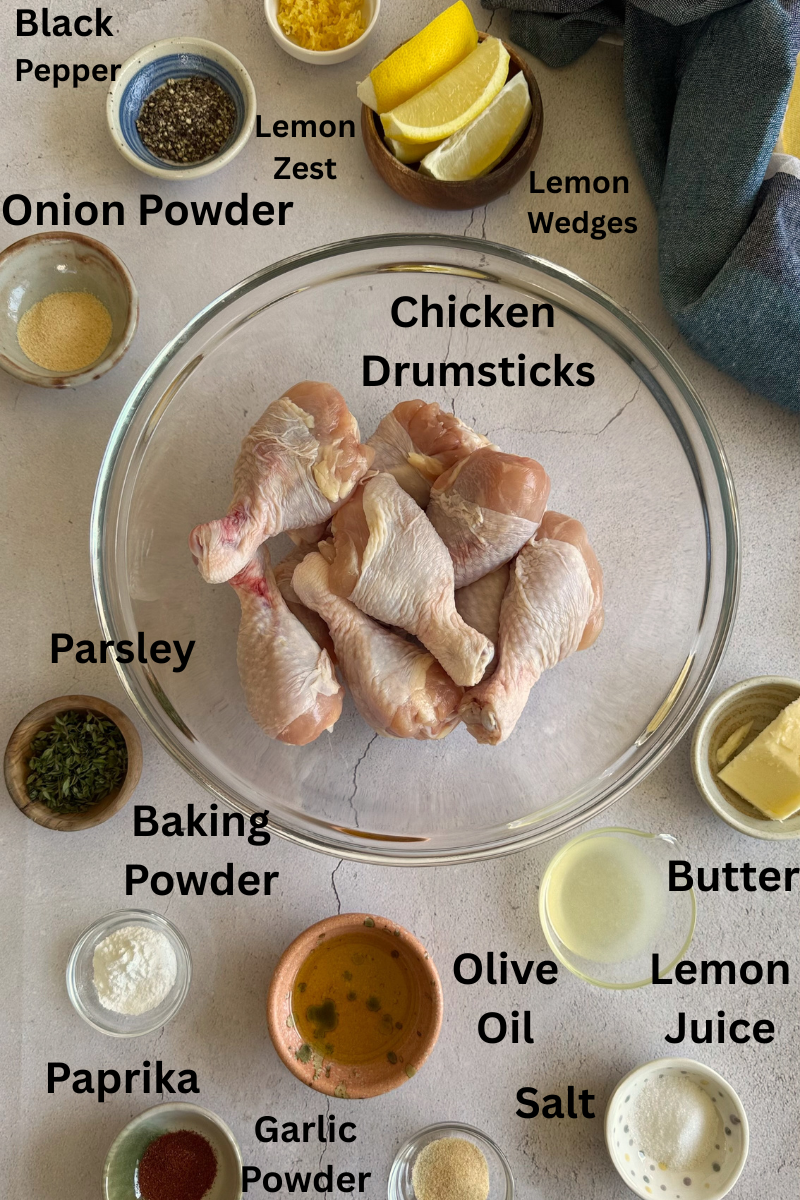 ingredients for lemon pepper chicken drumsticks - lemon zest, lemon juice, lemon wedges, chicken drumsticks, garlic powder, onion powder, black pepper, parsley, salt, baking powder, olive oil, and butter.