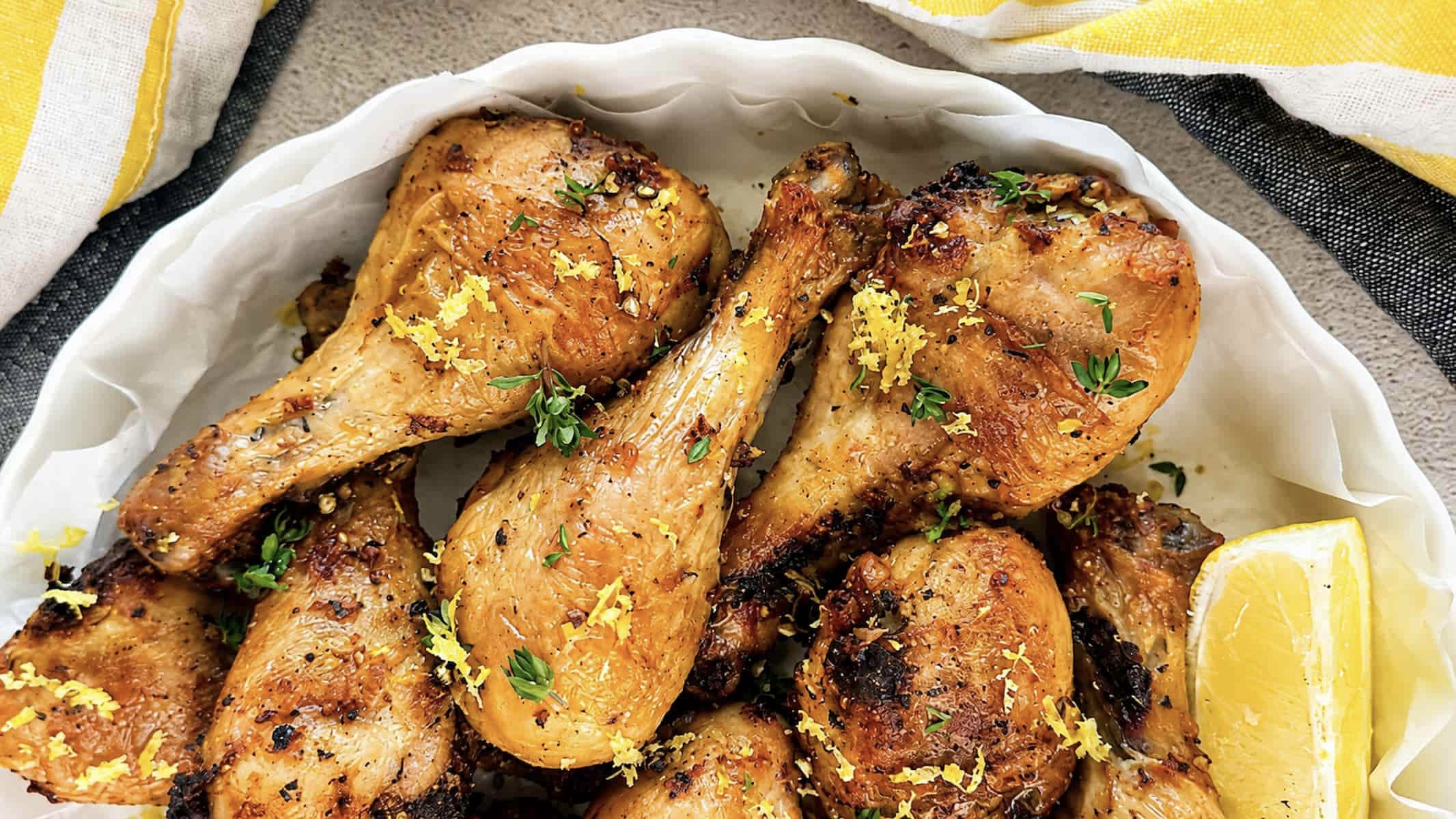 Lemon pepper chicken drumsticks with fresh thyme, lemon zest, and a lemon wedge.