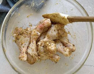 raw lemon pepper drumsticks in a glass bowl with a rubber spatula.