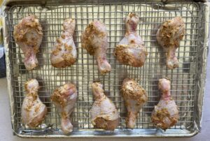 raw seasoned chicken drumsticks on a wire rack lined baking sheet.
