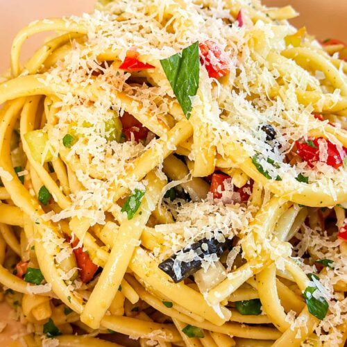 Linguine pasta salad with colorful vegetables, black olives, fresh herbs, and grated Parmesan cheese.