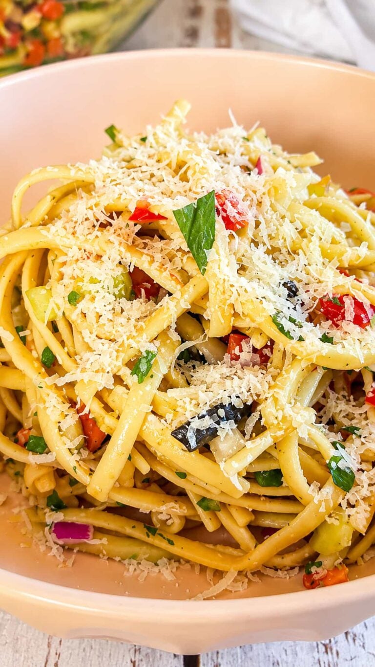 Linguine pasta salad with colorful vegetables, black olives, fresh herbs, and grated Parmesan cheese.