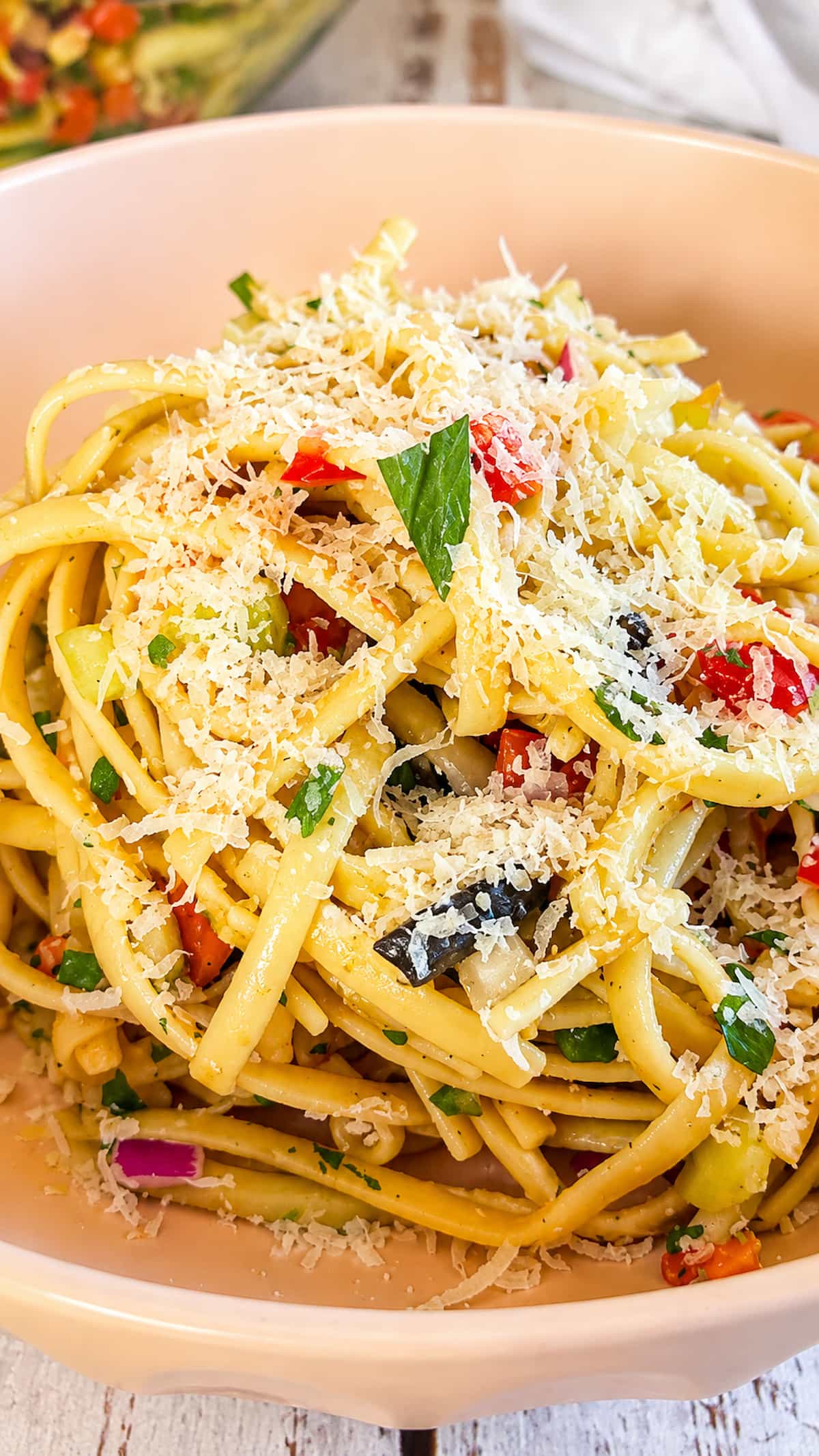 Linguine pasta salad with colorful vegetables, black olives, fresh herbs, and grated Parmesan cheese.