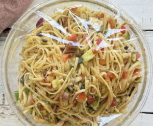 plastic wrap over a bowl of linguine pasta salad with veggies.