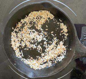 shredded coconut toasting in a small cast iron skillet on a burner.