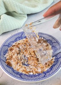 glass being rimmed with toasted coconut and salt by rolling in it in a blue plate.
