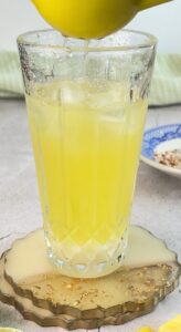 yellow cocktail being made in a glass with ice and lime juice being squeezed into it.