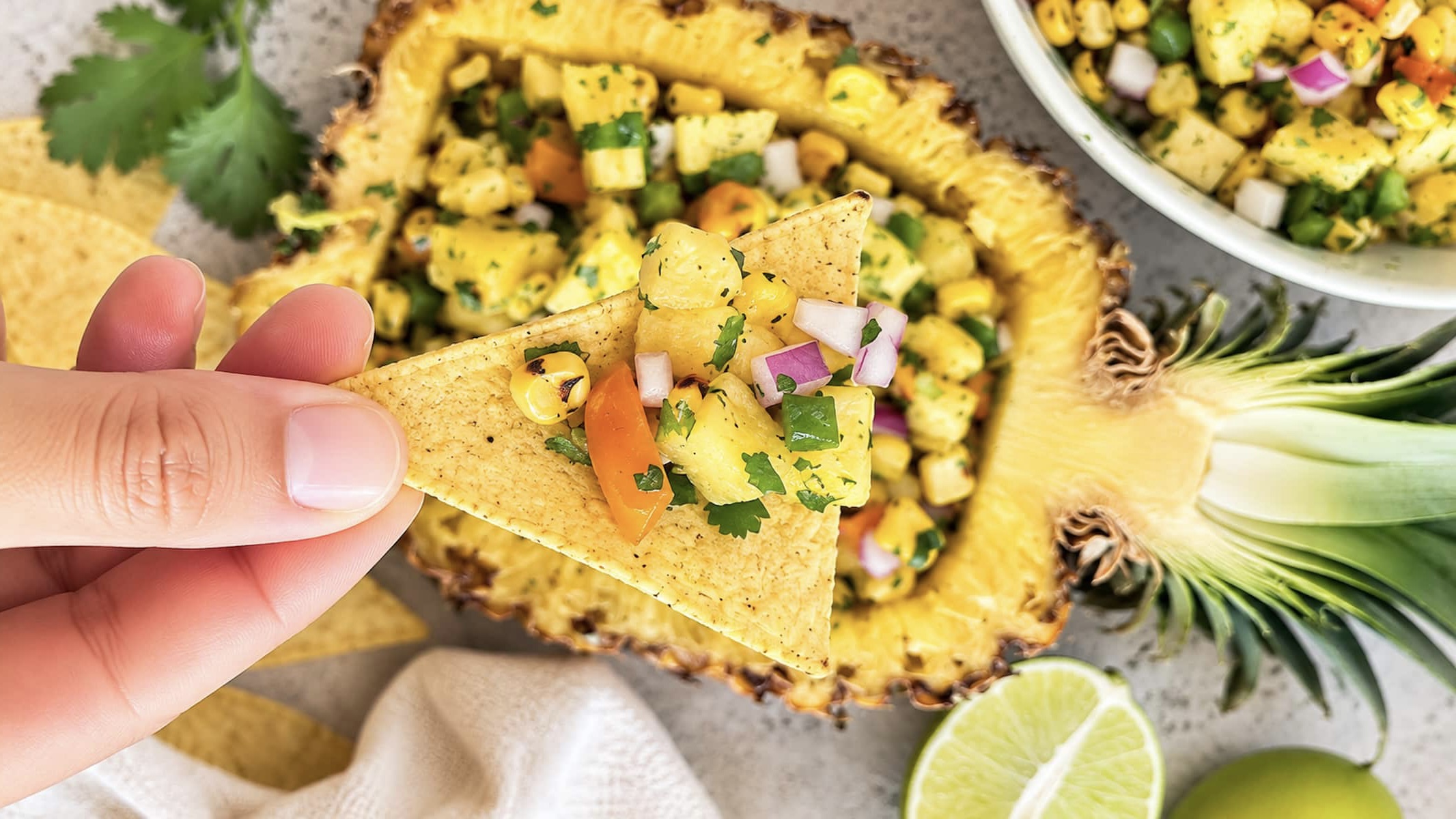 hand holding a tortilla chip with pineapple corn salsa on it over a pineapple loaded with more salsa.
