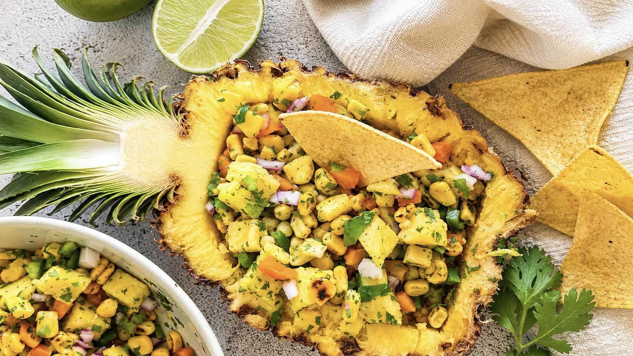 Pineapple corn salsa in a hollowed out pineapple with charred corn, fresh pineapple, red onion, peppers, cilantro, and tortilla chips.