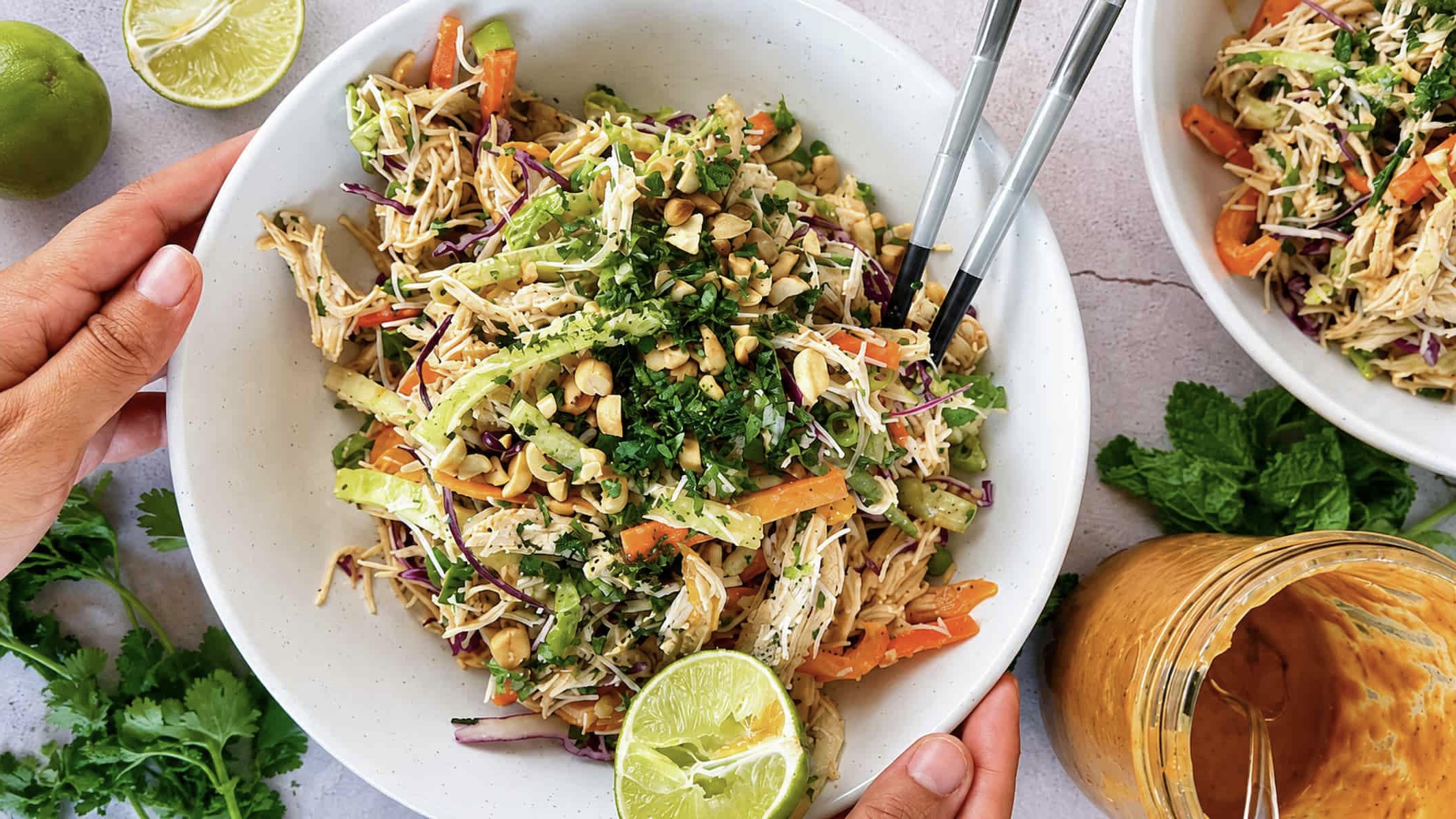 Thai chicken noodle salad with rice noodles, shredded chicken, crunchy vegetables, peanuts, fresh herbs, and lime in a serving bowl.