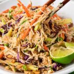 Thai chicken noodle salad with shredded chicken, rice noodles, crunchy vegetables, peanuts, and creamy peanut dressing lifted with chopsticks.