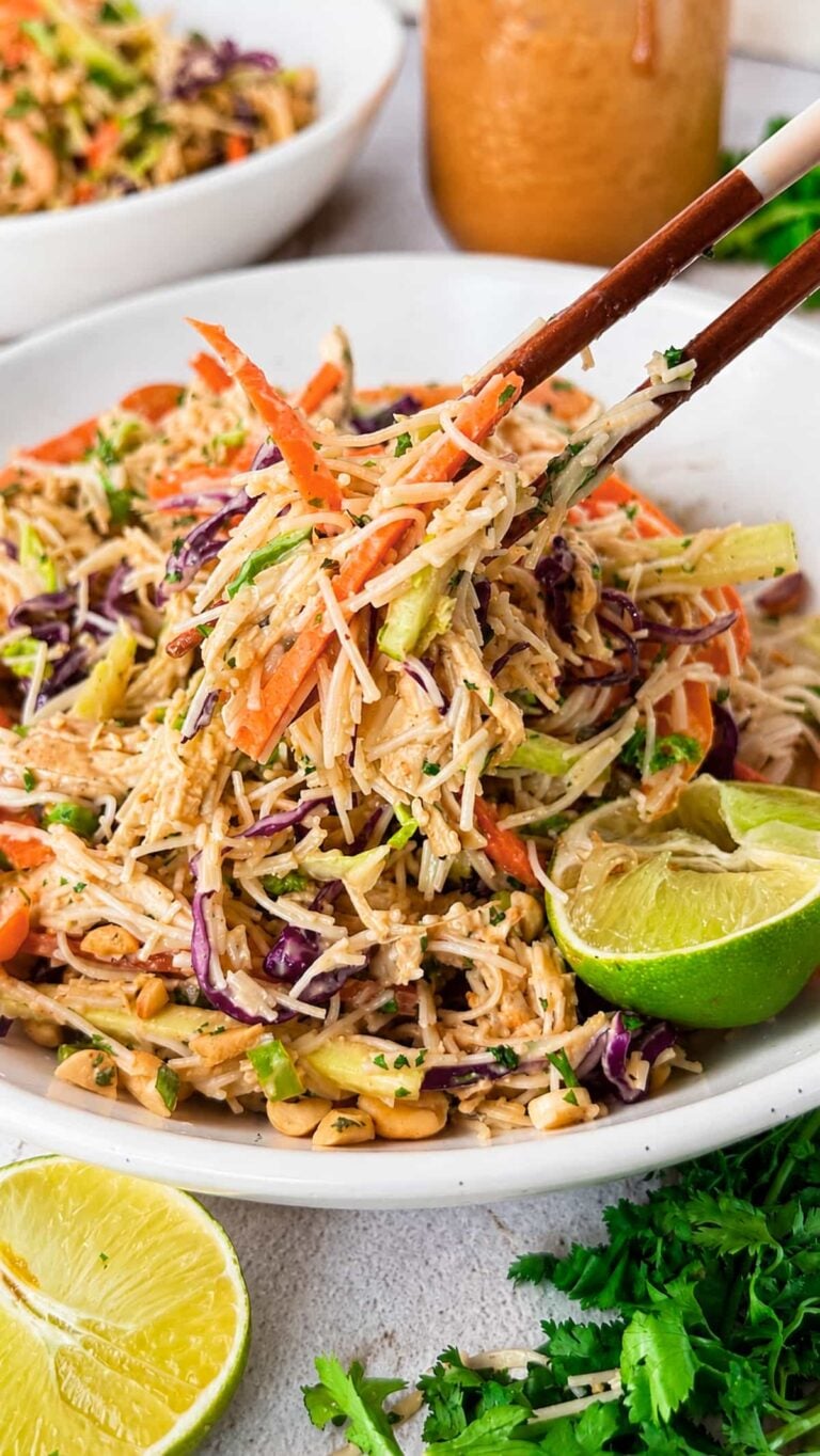Thai chicken noodle salad with shredded chicken, rice noodles, crunchy vegetables, peanuts, and creamy peanut dressing lifted with chopsticks.