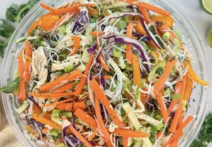 Thai chicken noodle salad in a glass bowl with rice noodles, shredded chicken, crisp vegetables, and fresh herbs.
