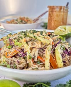 Thai chicken noodle salad with shredded chicken, rice noodles, crunchy vegetables, peanuts, and lime served with creamy peanut dressing.