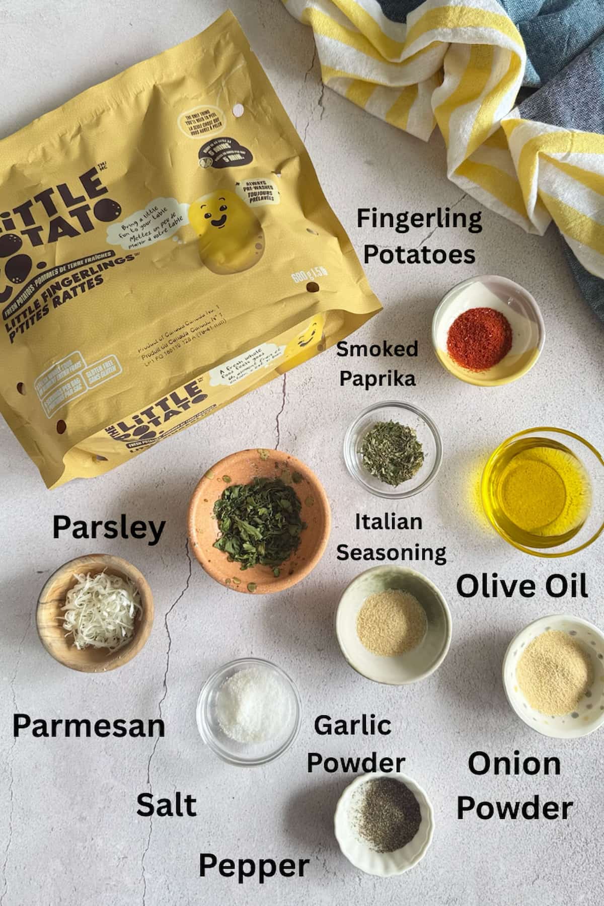 ingredients for air fryer fingerling potatoes laid out in separate bowls - bag of fingerling potatoes, olive oil, smoked paprika, parmesan, parsley, salt, pepper, onion powder, garlic powder, and italian seasoning.