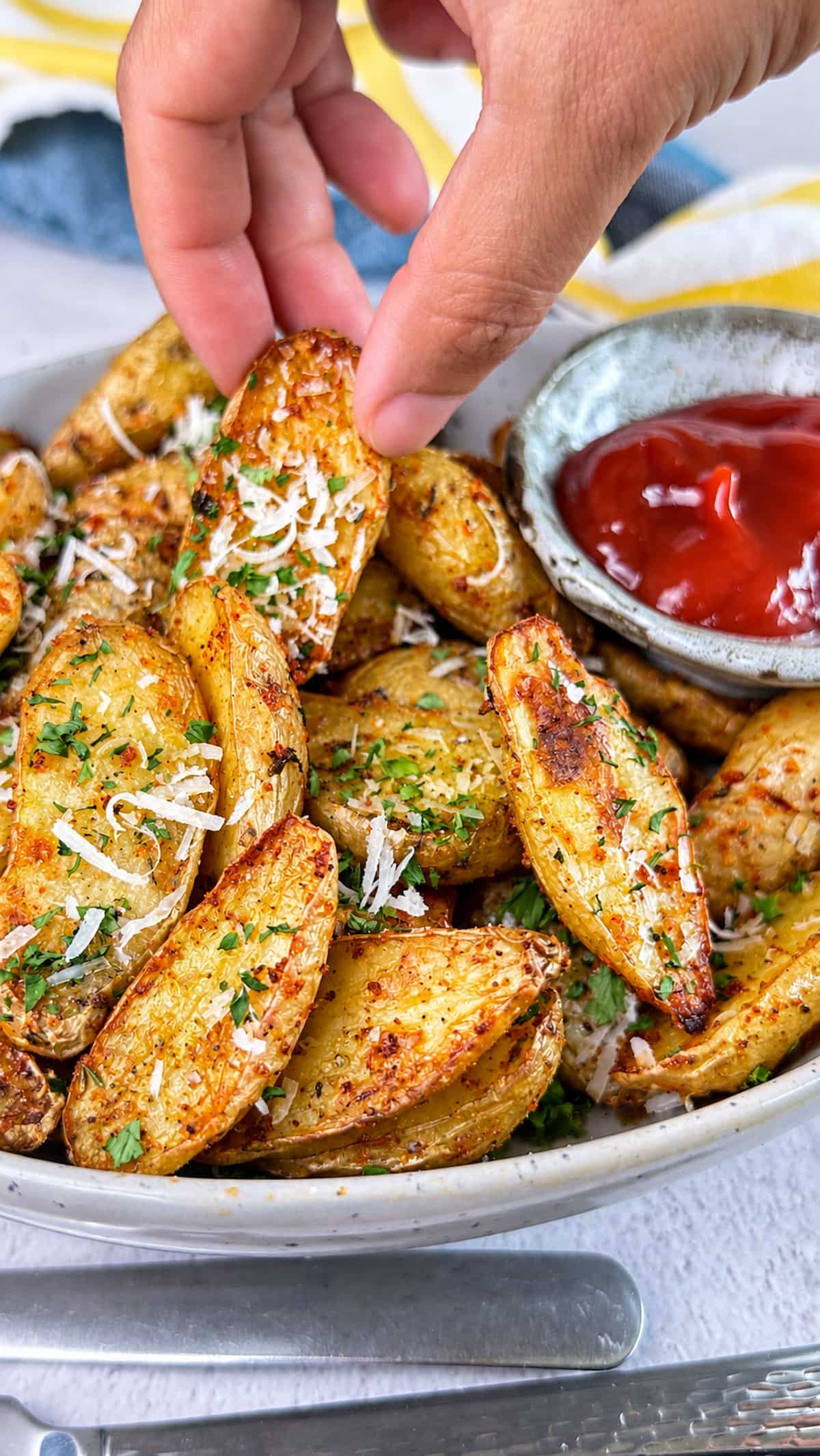 Hand picking up a crispy Parmesan air fryer fingerling potato from a bowl of golden roasted potatoes.