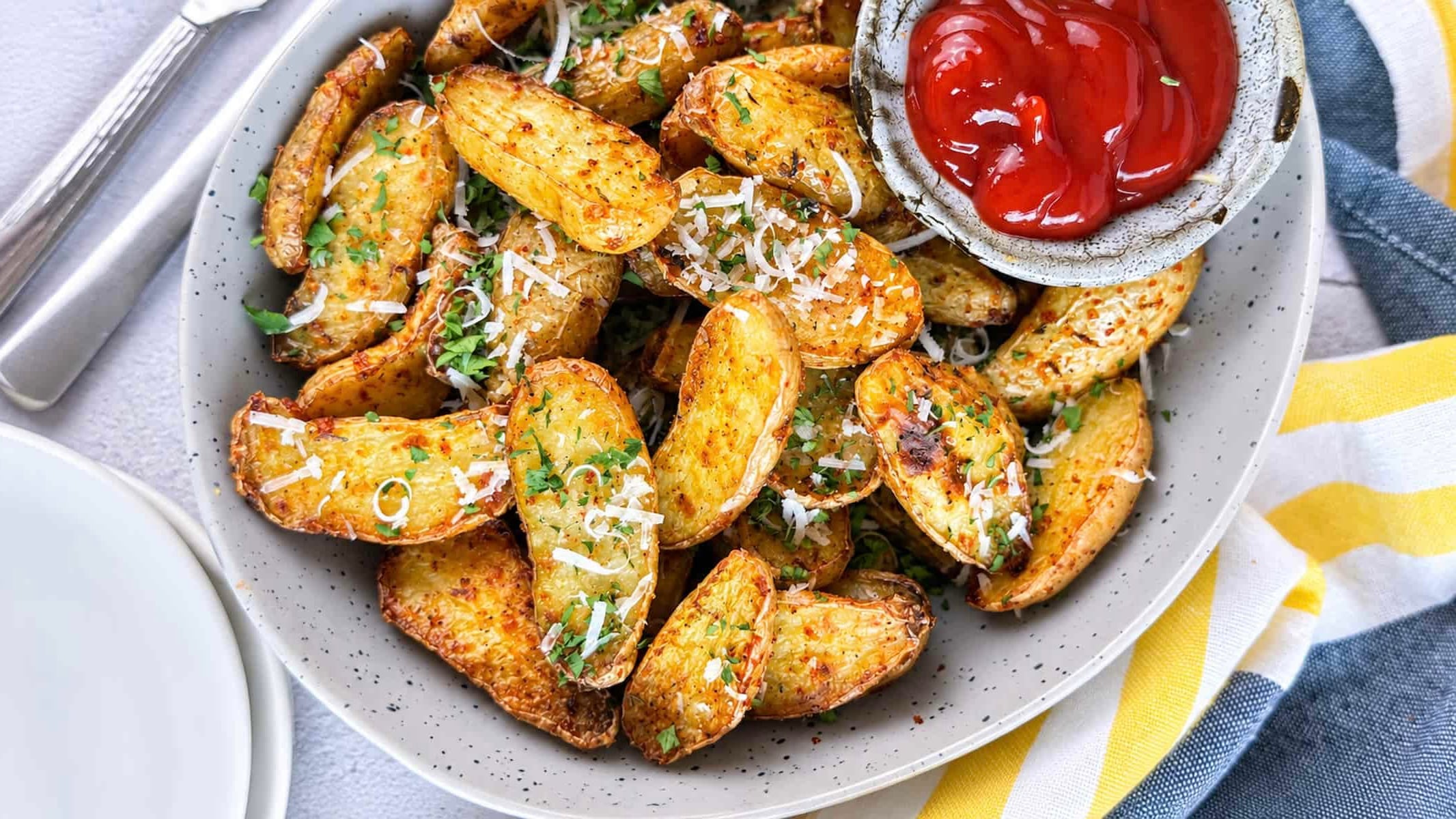 Crispy air fryer fingerling potatoes topped with Parmesan and fresh parsley, served with ketchup for dipping.