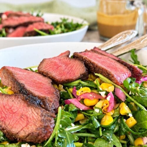 Arugula steak salad topped with juicy sliced steak, sweet corn, pickled red onions, crumbled cheese, and a creamy homemade dressing.